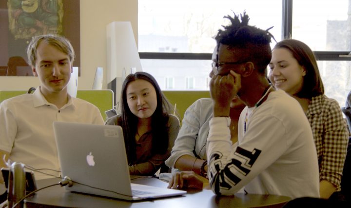 Students gather around a laptop computer listening to a podcast