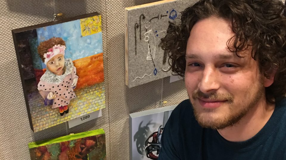 A picture of Oliver Hollocher-Small in front of a wall containing art.