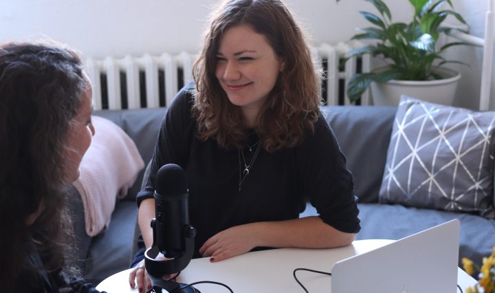 2 women sitting in front of a microphone and laptop, interviewing each other for a podcast