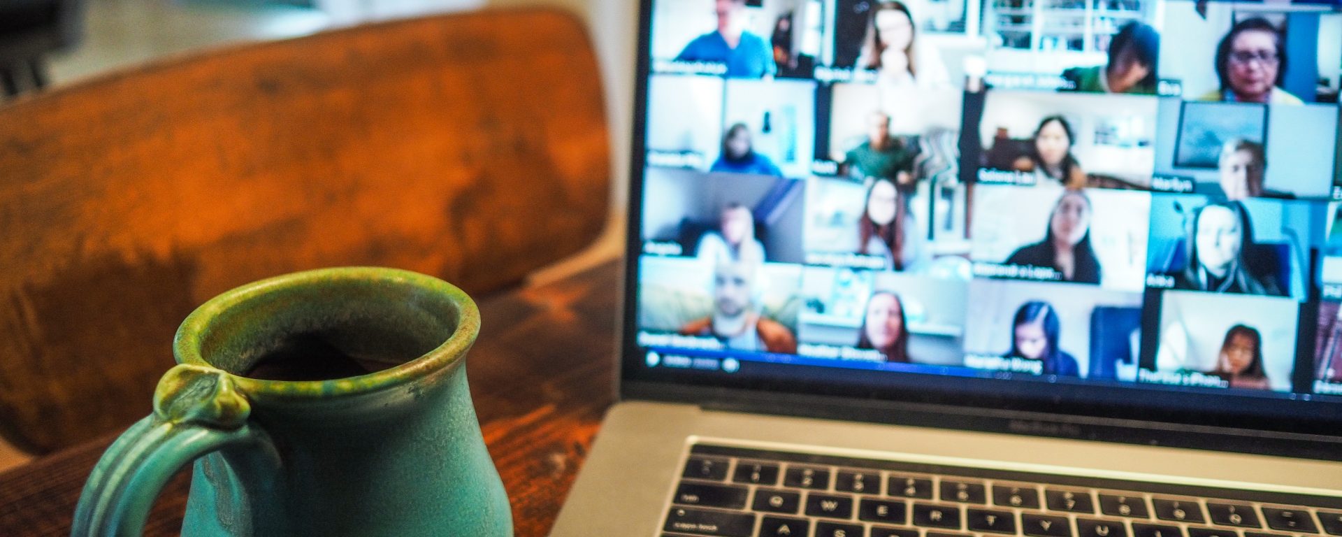 laptop showing many people in small windows on a zoom call with a blue coffe mug to the left