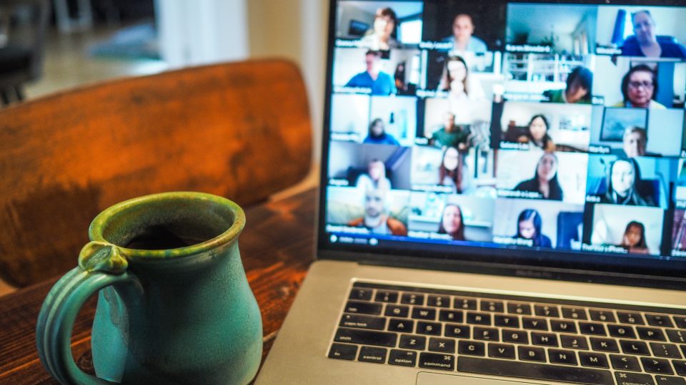laptop showing many people in small windows on a zoom call with a blue coffe mug to the left