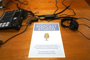 A sign promotes the Language & Media Centers PODCAST STUDIO, For help getting started visit: www.rode.com/interfaces-mixers/rodecaster-pro/learning-hub For questions email: lmc@swarthmore.edu. An audio mixer and heqadphones rest on the table next to the sign.