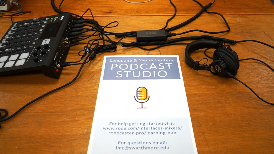 A sign promotes the Language & Media Centers PODCAST STUDIO, For help getting started visit: www.rode.com/interfaces-mixers/rodecaster-pro/learning-hub For questions email: lmc@swarthmore.edu. An audio mixer and heqadphones rest on the table next to the sign.
