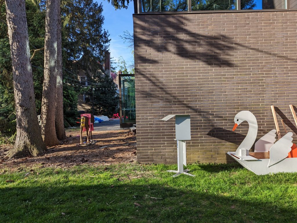 an image of an exterior wall of the Makerspace on a sunny day with a boat-sized wooden swan sitting in the grass in the foreground