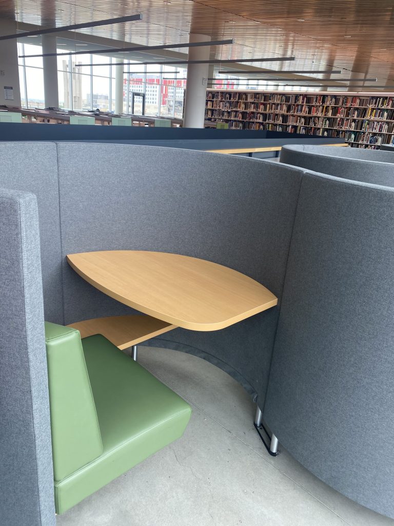 Individual study pod located in Charles Library. The walls of the pod are grey-blue and create an S-curve so that the next study pod sits in a connected piece of the wall. The seat is a natural green with a birch-tree-colored wooden desk. 