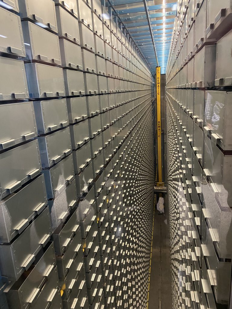 Charles Library's Bookbot retrieves a book from the storage. There are stories of metal boxes on either side with a yellow pole in the middle which can remove these metal boxes. The length looks like a half of a city block.