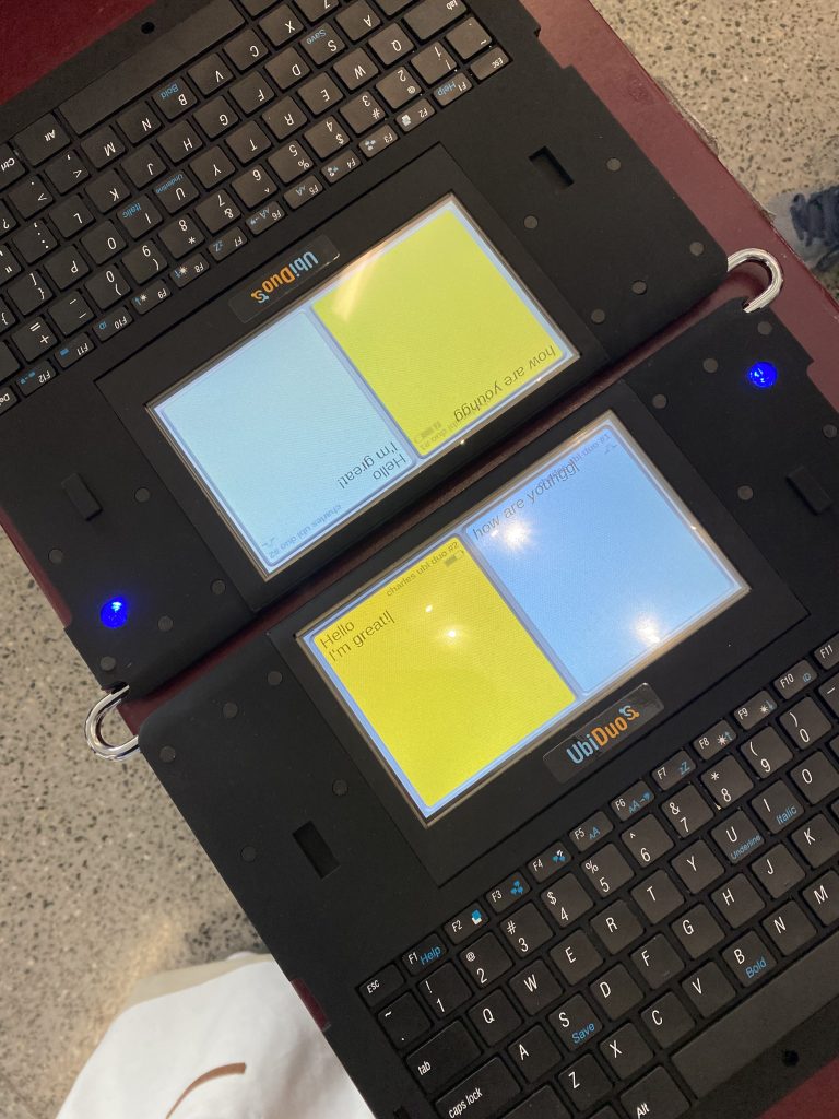 Ubiduo2 in use. A keyboard is below a small, split screen of yellow and blue. This is mirrored on the other side of the device so that folks can type to each other in real time.