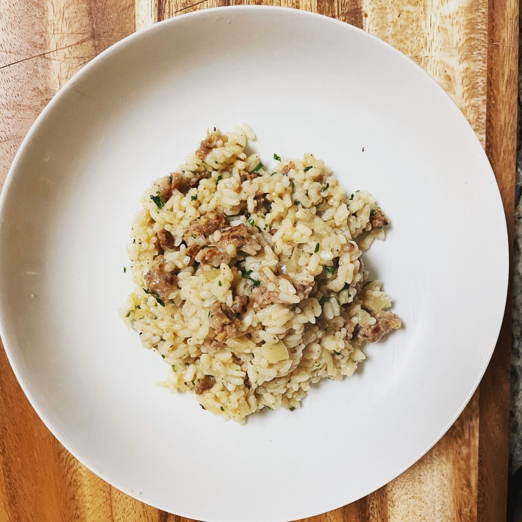 Overhead shot of a plate of risotto with ground meat and herbs, served on a white plate, placed on a wooden cutting board.
