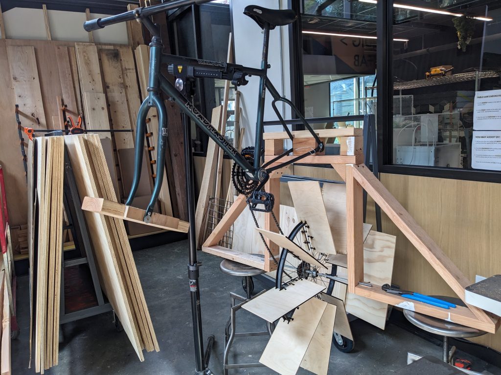 a deconstructed bicycle with wood structures attached, in progress toward being made into a pedal-powered boat