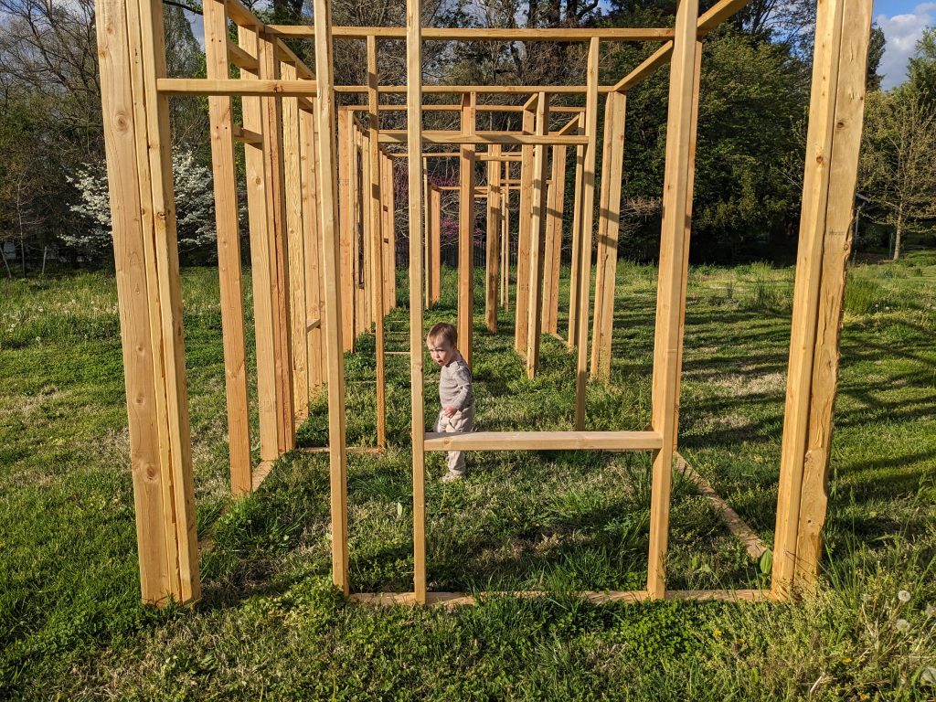 a wood frame in a grassy open space with a toddler wandering through