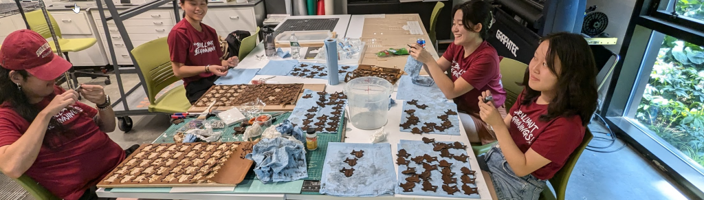 a photograph of four students working on leather keychains together at a table