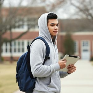 Male student with a backpack and hoodie, holding a laptop computer