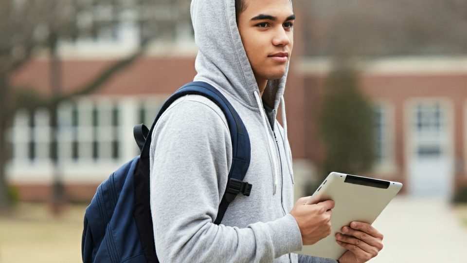 Male student with a backpack and hoodie, holding a laptop computer