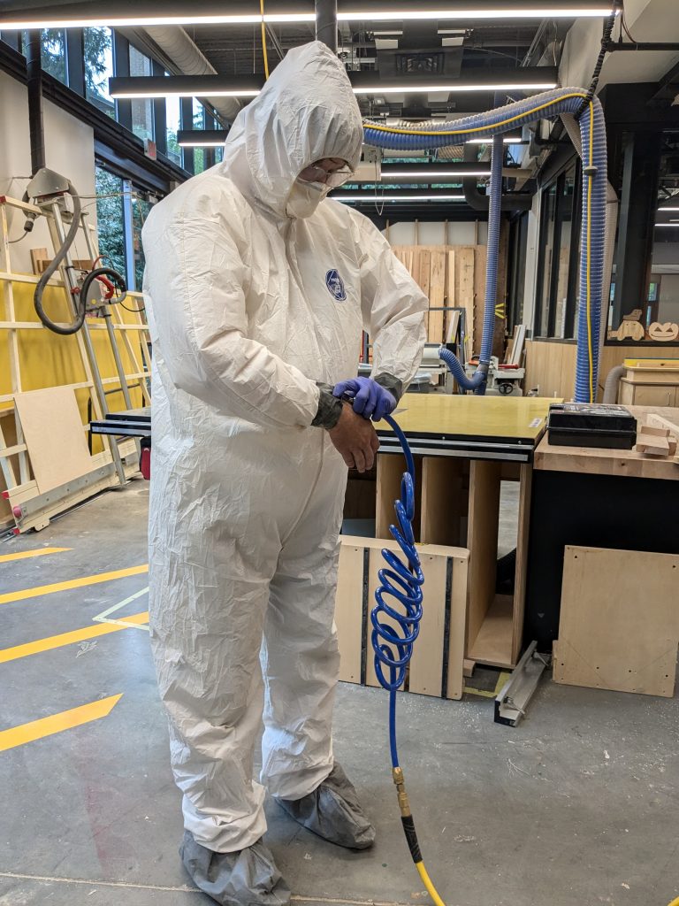 full-body shot of the makerspace manager in tyvek coveralls, inflating his suit with compressed air