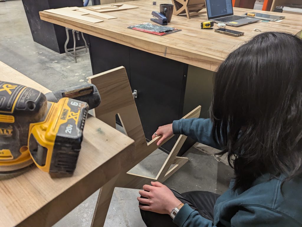 a downward-looking view of an art student holding up a shaped piece of plywood