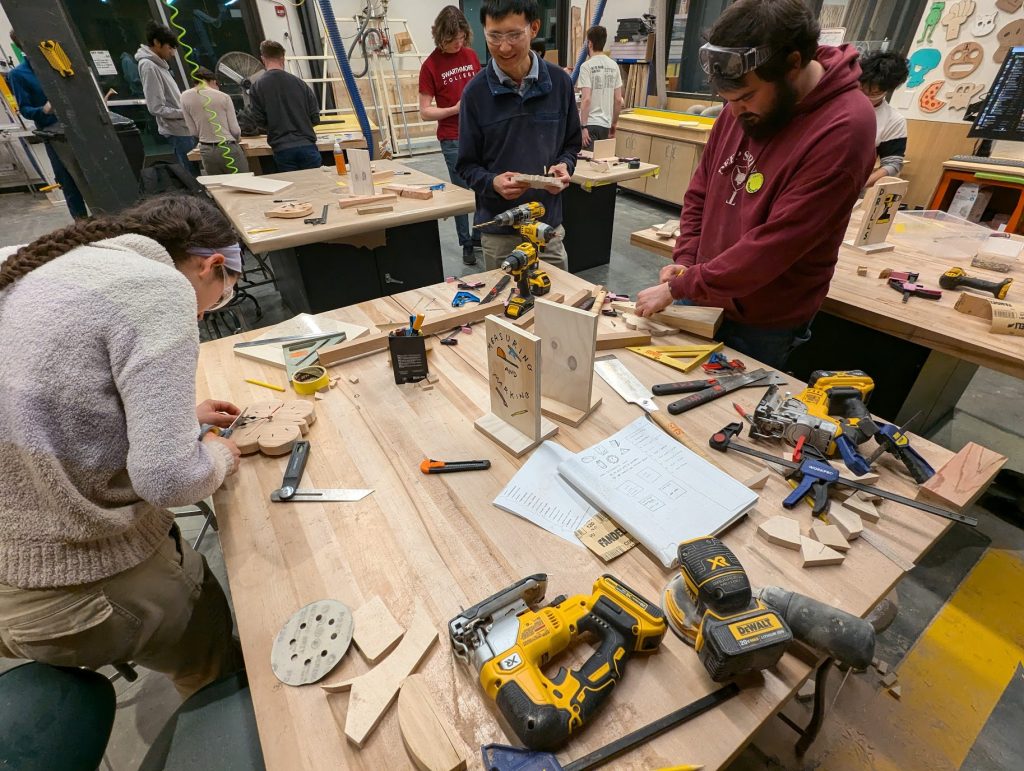 an overhead shot of a handful of students working around a table in a woodshop with tools and materials spread out