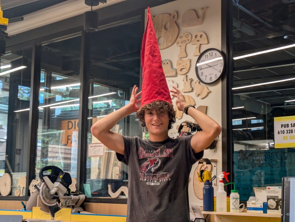 A happy student holding a handmade red gnome hat on his head for the camera