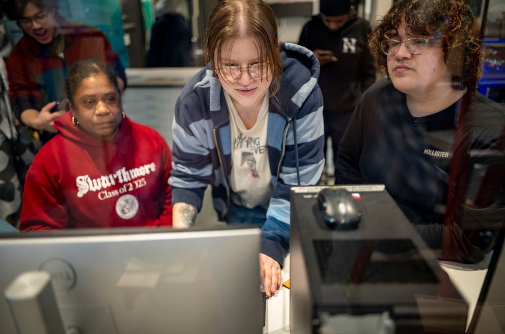 Two students and a staff member huddle around a computer monitor working on a project together