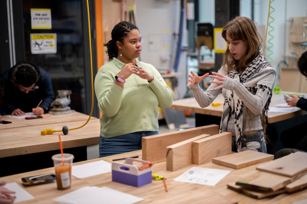 a student working in the makerspace gesticulates an idea to a workshop participant who listens