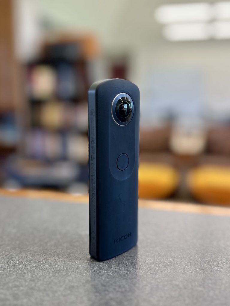 Ricoh Theta 360 camera standing upright on a table