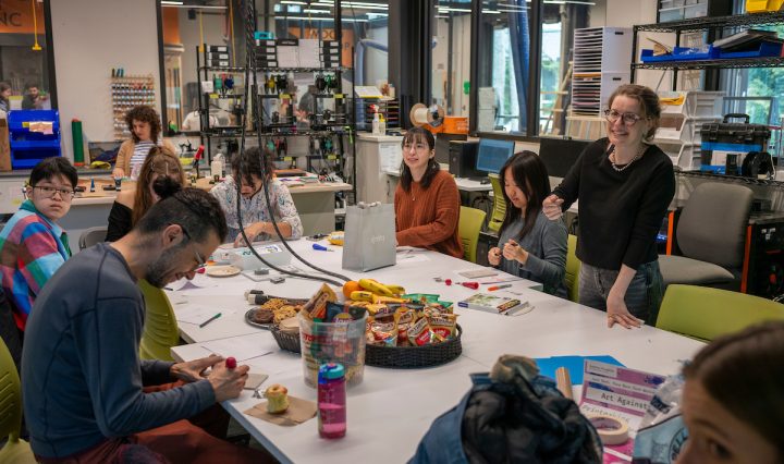 Students participate in an “Art Against AI” stamp-making workshop in Swarthmore College’s MakerSpace, gathered around worktables with art supplies and refreshments as facilitator Linda Huber leads the activity.