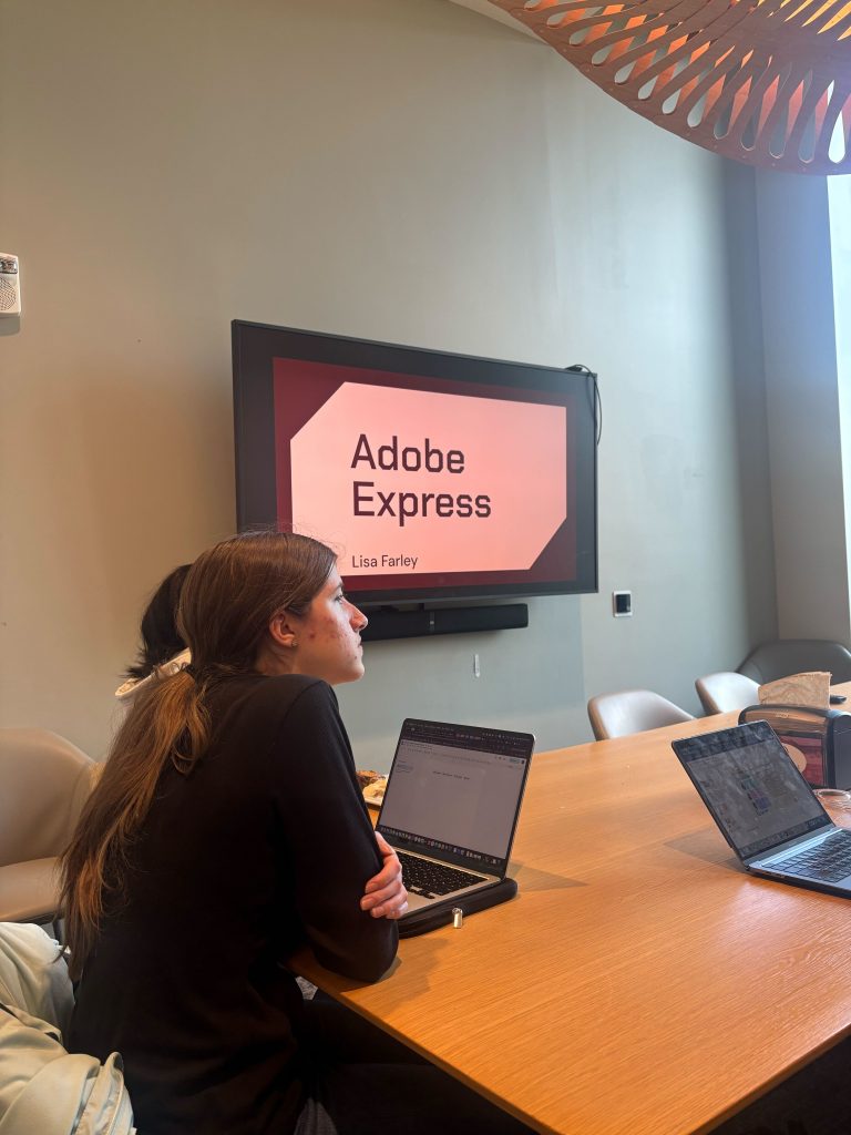 Students sit around a dinner table with a presentation on Adobe Express on display. 