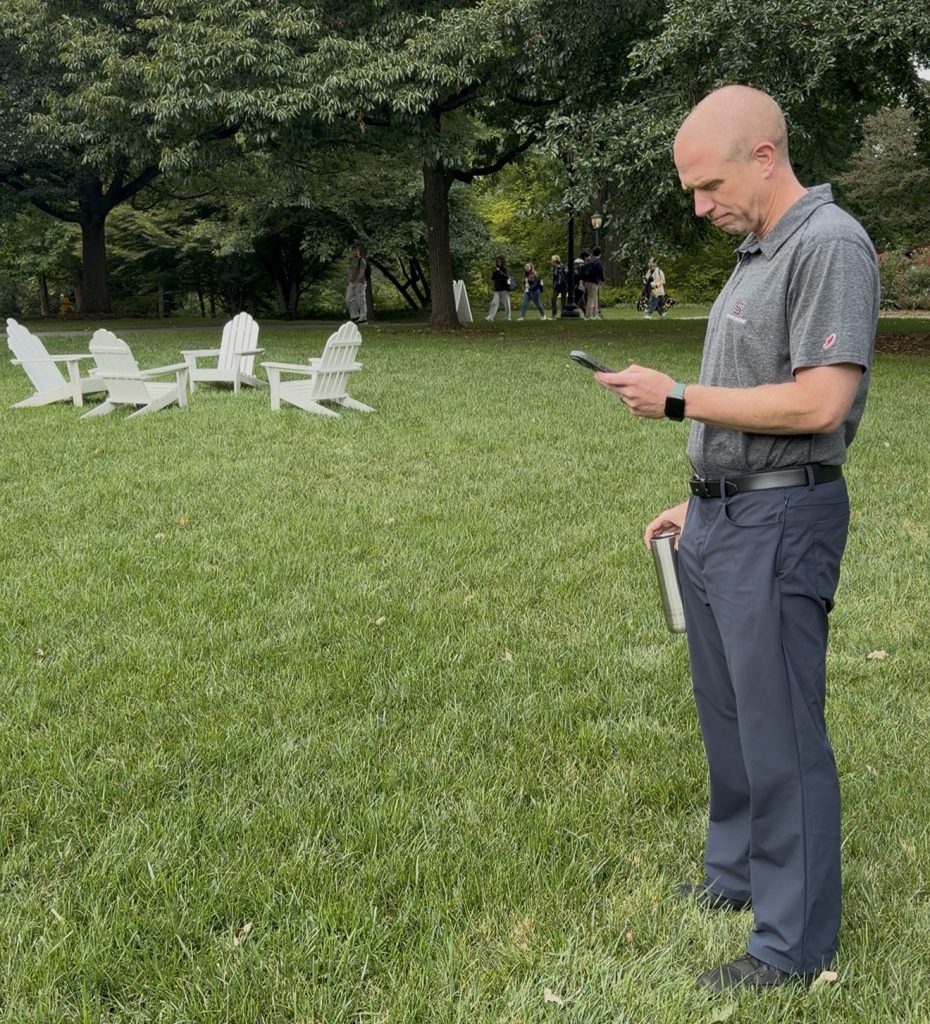 Bill stands at the top of Parrish Beach scrolling on his cell phone